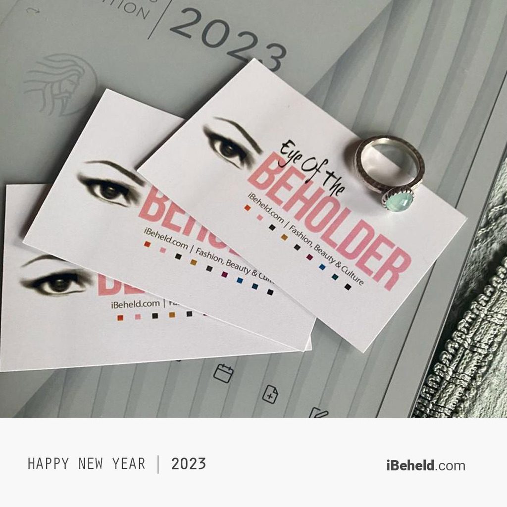 PICTURE SHOWS THREE EYE OF THE BEHOLDER BUSINESS CARDS LYING ON A DIGITAL PLANNER. A SILVER RING SET WITH A ROUND MILKY BLUE STONE LIES ALONGSIDE THEM. JUST VISIBLE IN THE LOWER RIGHT EDGE OF THE PHOTO: EMBELLISHED FABRIC, THE SAME COLOUR AS THE STONE IN THE RING. THE STONE IS AQUA CHALCEDONY.