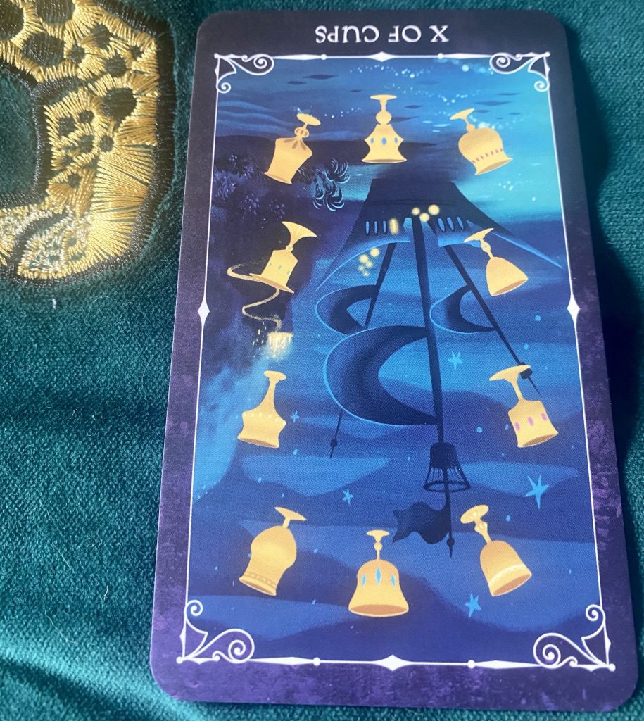 Golden chalices encircle a pirate ship seen in sillouhette against a midnight blue sea and sky ten ot chalices reversed from Disney Villains tarot deck