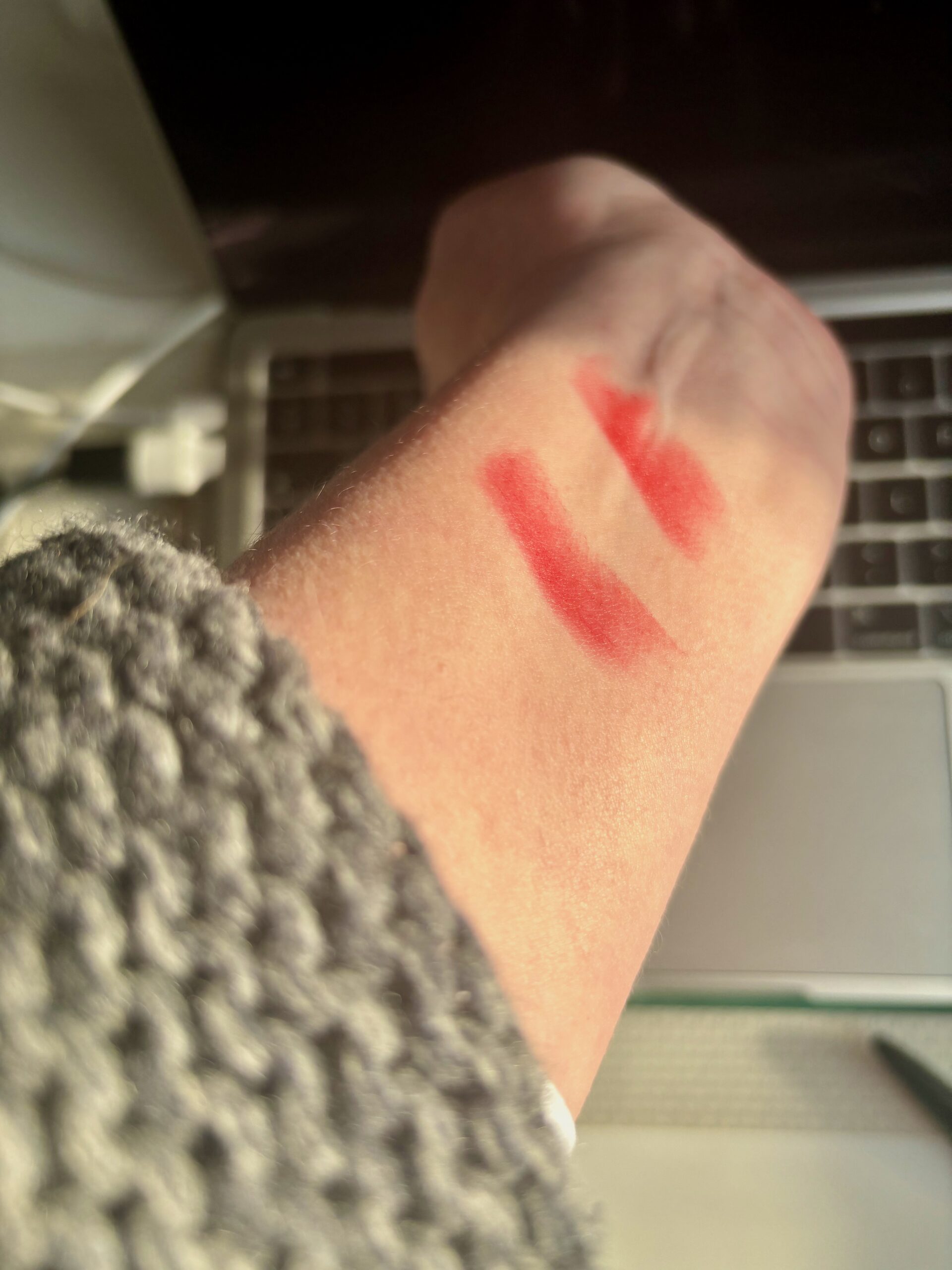La Rouge Bouche Folie and Rouge Mat 21 swatched on a wrist, photographed in sunshine