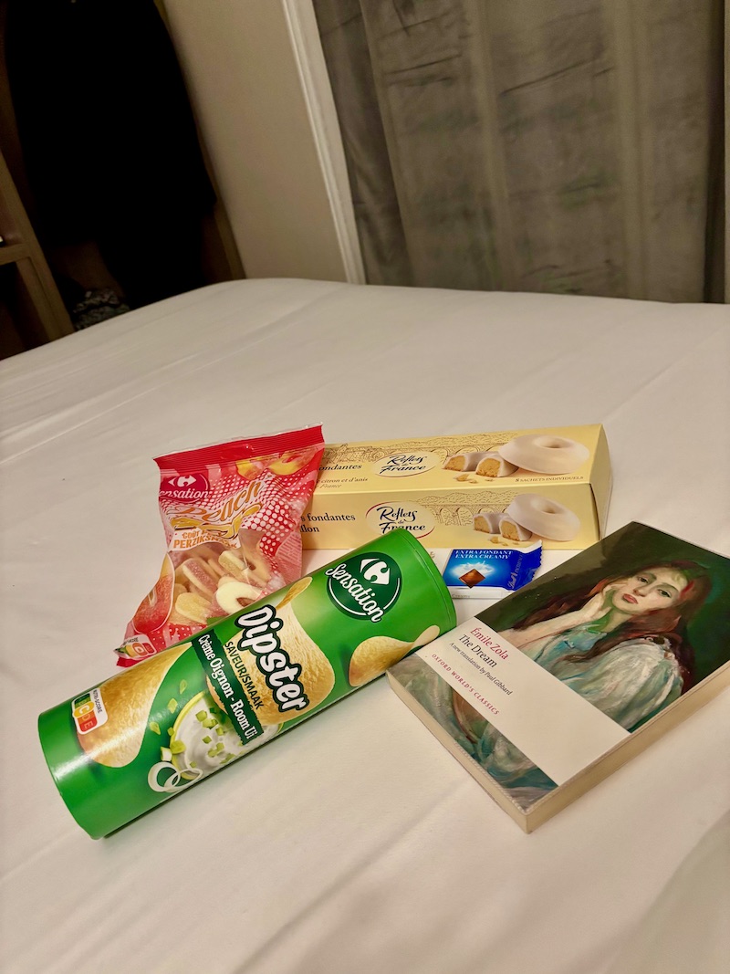 French snacks on a hotel bed, with a copy of Zola's The Dream