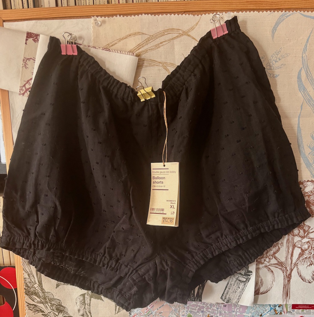 MUJI Balloon Shorts pinned up with bulldog clips against a cork pinboard full of wallpaper samples